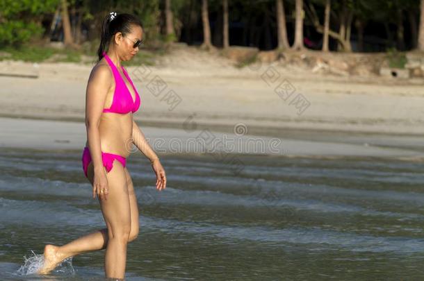 女人形状大大地走向海滩和粉红色的比基尼式游泳衣