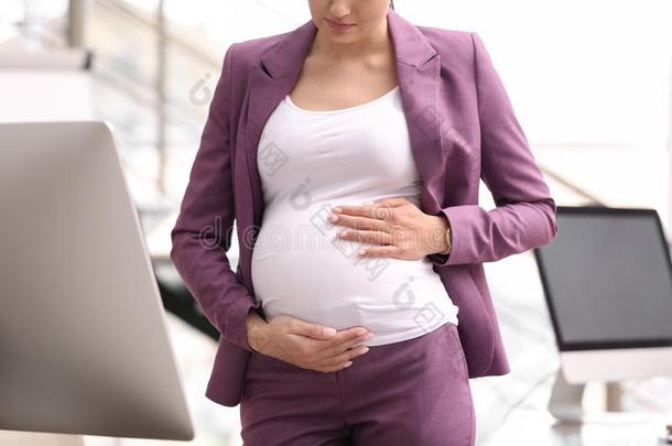 年幼的怀孕的女人采用一套外衣在工作场所