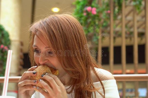 饥饿的女孩吃汉堡包向食物法院.女人尖锐刺人的芝士面包