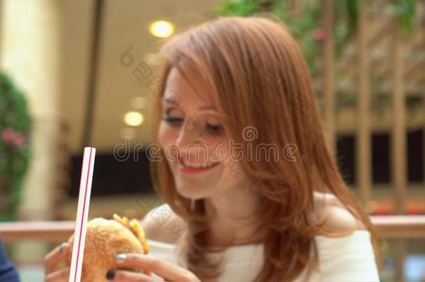 饥饿的女孩吃汉堡包向食物法院.女人尖锐刺人的芝士面包