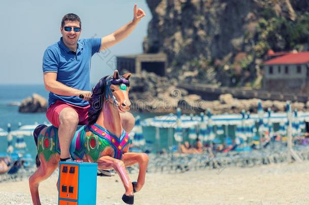 闹着玩的疯狂的男人爸爸骑马木制的摇摆的马在海滩,哈普