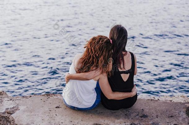 两个女人朋友一次在旁边指已提到的人海滩热烈地拥抱.生活方式康塞普