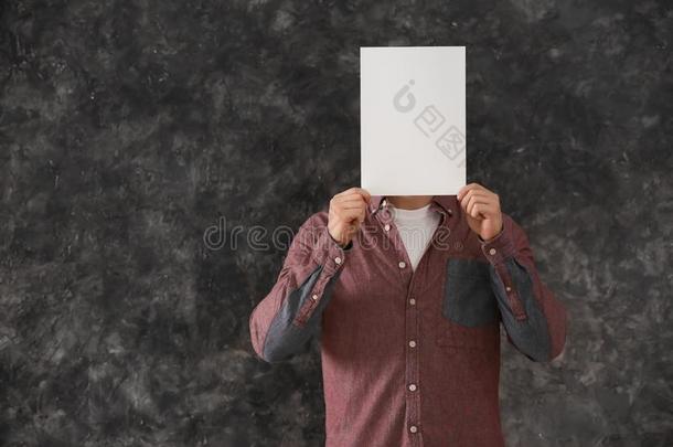 年幼的男人躲藏面容在的后面空白的纸关于纸向灰色的后面