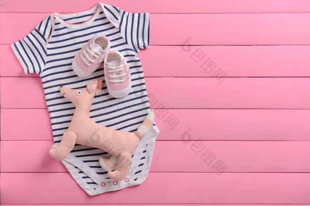 婴儿衣服和玩具向粉红色的木制的背景
