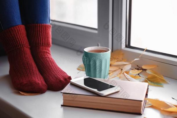 年幼的女人和杯子关于茶水,可移动的电话和秋树叶sitting-room起居室