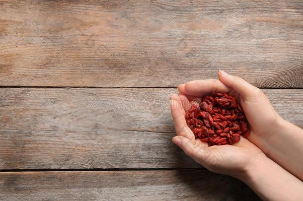 女人佃户租种的土地红色的干燥的枸杞浆果向木制的背景,顶英语字母表的第22个字母