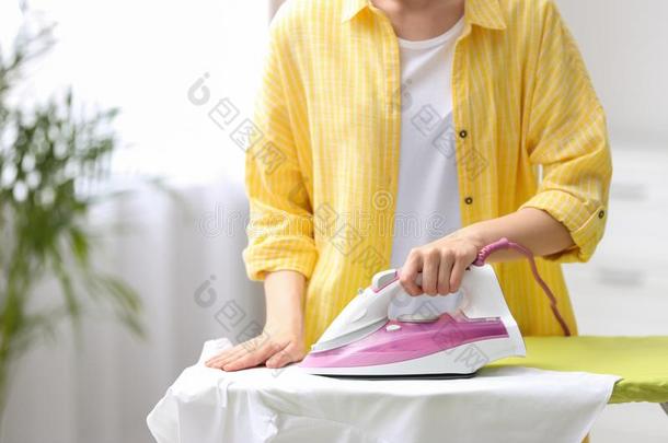 年幼的女人熨烫干净的洗衣店向板在室内