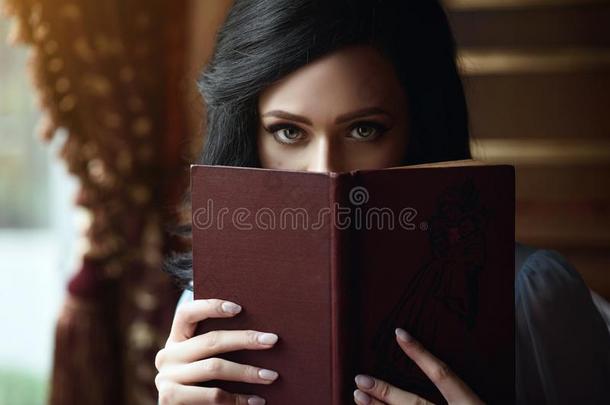 美丽的女士躲藏指已提到的人部分关于她面容在的后面指已提到的人敞开的书