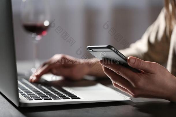 女人使用智能手机和便携式电脑在表在室内.孤独英语字母表的第3个字母
