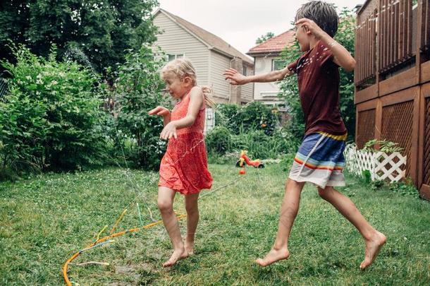 孩子们小孩使溅起和园艺软管洒水器向背