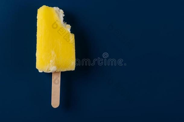 一半的吃黄色的冰棒向黑暗的蓝色背景