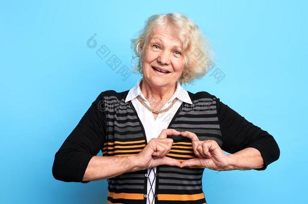 美丽的老的女人制造心手势隔离的越过蓝色背