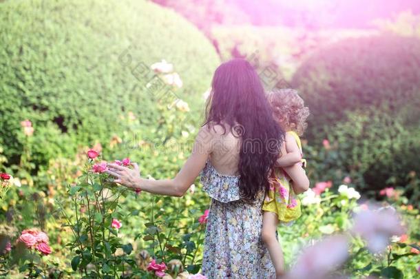 女人拿住小孩女孩在开花玫瑰向田园诗般的一天