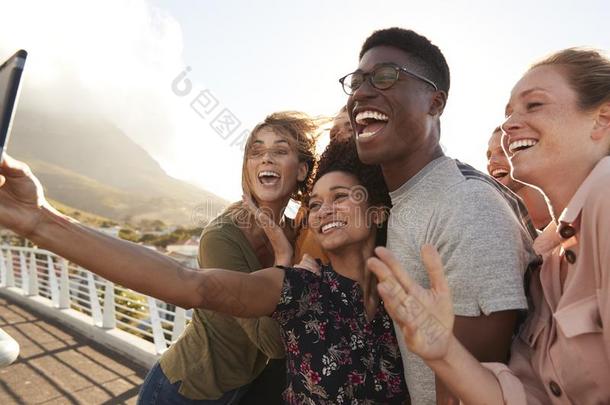 微笑的年幼的朋友使摆姿势为自拍照向户外的人行桥向