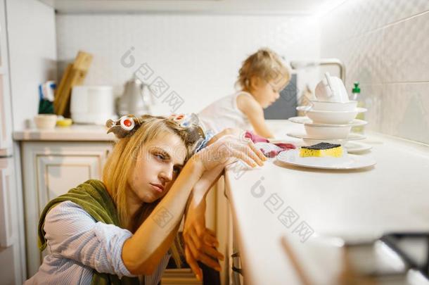 小的女孩洗涤盘在近处疲倦的家庭主妇
