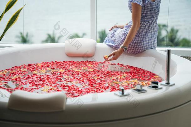 年幼的女人令人轻松的向奢侈浴缸和玫瑰树叶