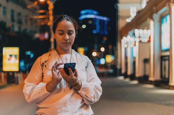 年幼的漂亮的女孩使用可移动的电话或smart电话向夜城市