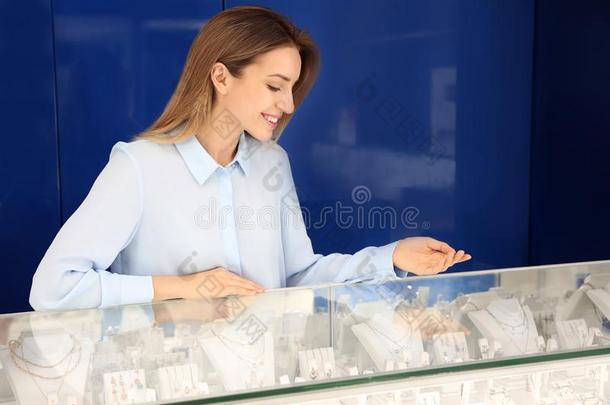 肖像关于年幼的女售货员在近处玻璃<strong>柜台</strong>采用珠宝