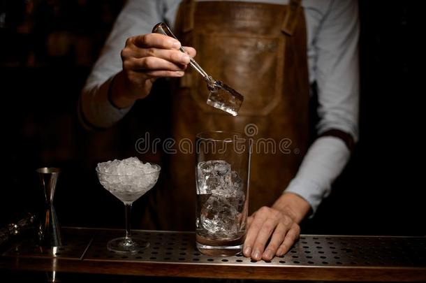 酒吧间销售酒精饮料的人放冰采用鸡尾酒玻璃和V形夹子