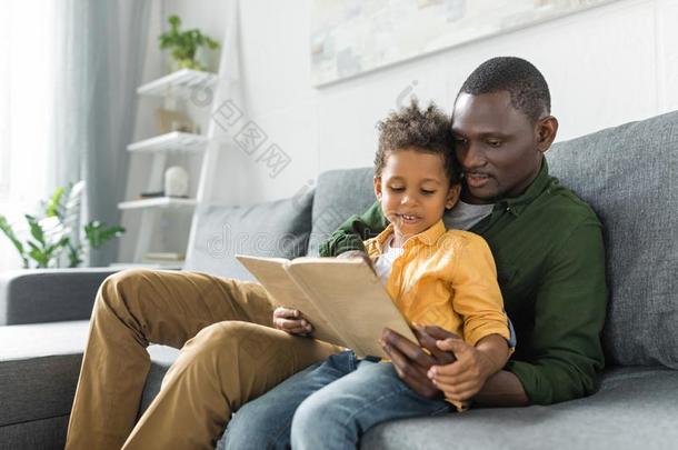 轻松的非洲的-美国人父亲和儿子阅读书同时