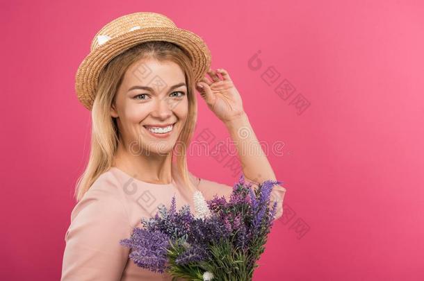 美丽的幸福的女人使摆姿势采用稻草帽子和花束关于花