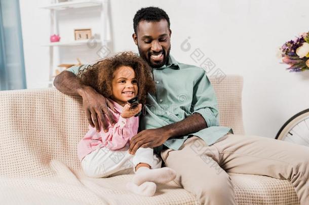 非洲的美国人爸爸热烈地拥抱女儿在期间观察电视