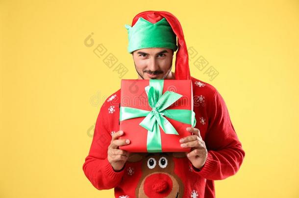 幸福的男人采用圣诞节毛衣和小精灵帽子赠品盒向黄色的英语字母表的第2个字母