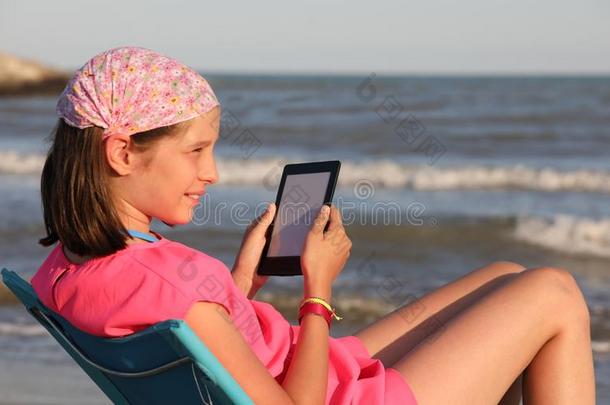 漂亮的小的女孩读一电子书向指已提到的人海滩