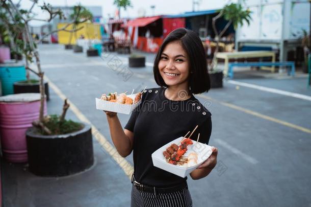 亚洲人年幼的女人运送的一大街食物烤的