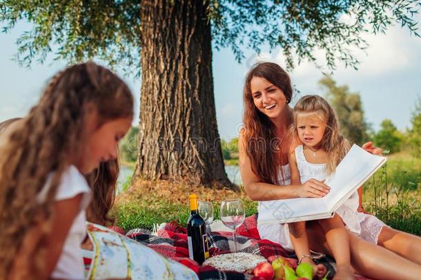 母亲和小孩阅读书在户外.家庭所有野餐郊游采用