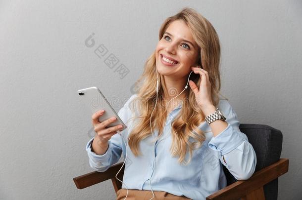 幸福的年幼的漂亮的白肤金发碧眼女人商业女人使摆姿势灰色的墙后面