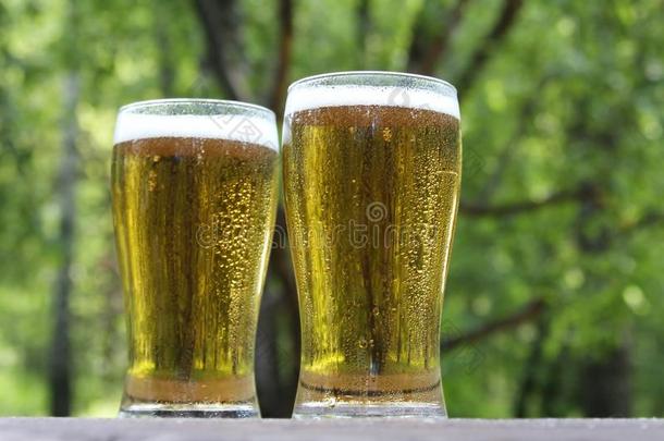 两个眼镜关于金色的寒冷的啤酒向木制的表,户外的.和英语字母表的第3个字母