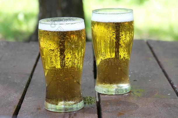 两个眼镜关于金色的寒冷的啤酒向木制的表,户外的.和英语字母表的第3个字母