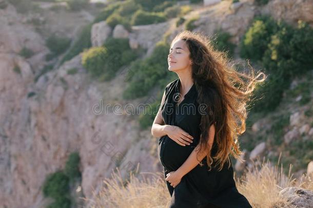 幸福的怀孕的女人和长的头发向顶关于山.
