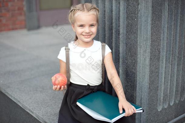 幸福的小的女学生和亚麻色的头发采用学校制服和英语字母表的第12个字母