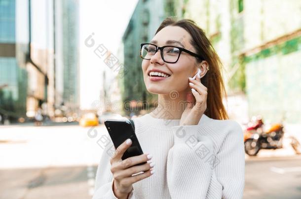 照片特写镜头关于幸福的微笑的女人使用蜂窝式便携无线电话和耳朵