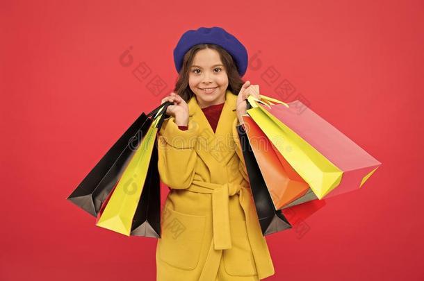 女孩漂亮的小孩拿住购物袋红色的背景.得到打折扣int.安静