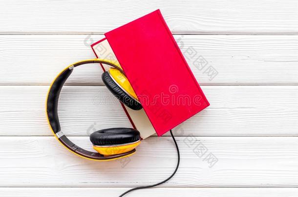 倾听向听觉的书和戴在头上的收话器向白色的木制的背景