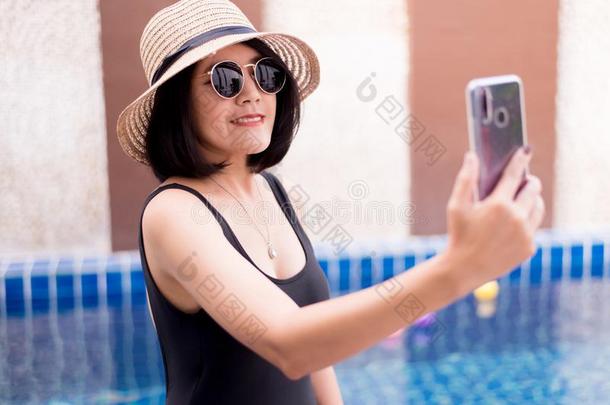 美丽的亚洲人女人自拍照和可移动的电话在游泳水池,