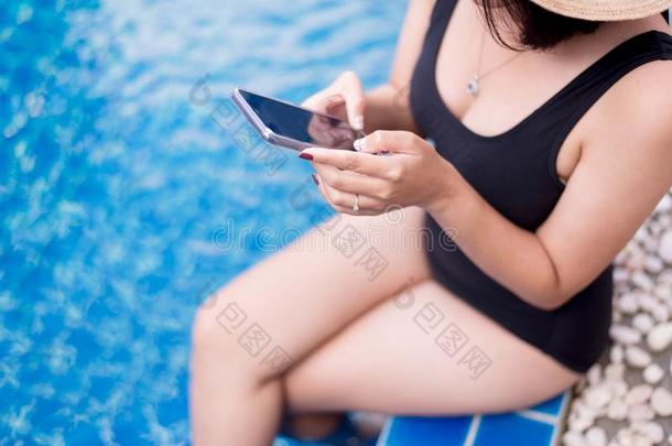 美丽的亚洲人女人使用可移动的电话在游泳水池,幸福的