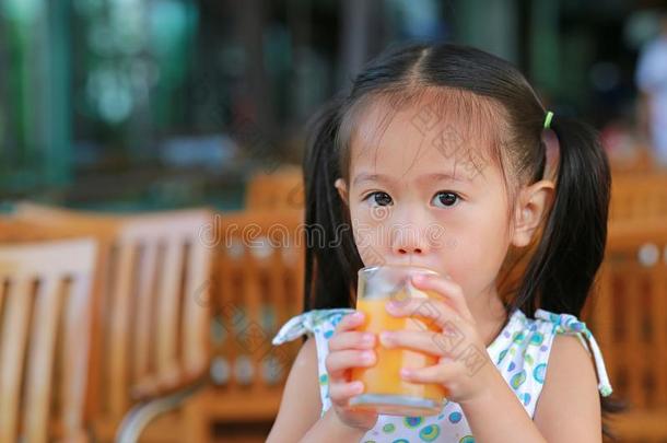 特写镜头关于小的女孩喝饮料桔子果汁和有样子的照相机