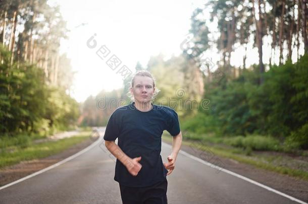 高加索人年幼的有卷发的男人运动员跑和煦的：照到阳光的夏一天向沥青油