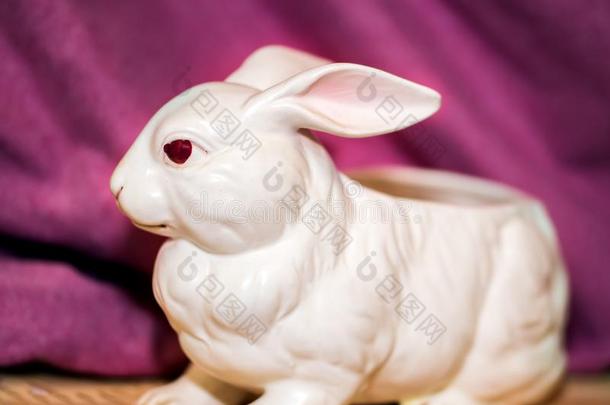 白色的陶器的兔子和红色的眼睛向粉红色的背景和木制的