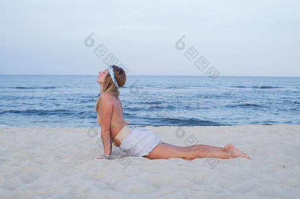 年幼的女人开业的瑜伽向指已提到的人海滩.眼镜蛇使摆姿势