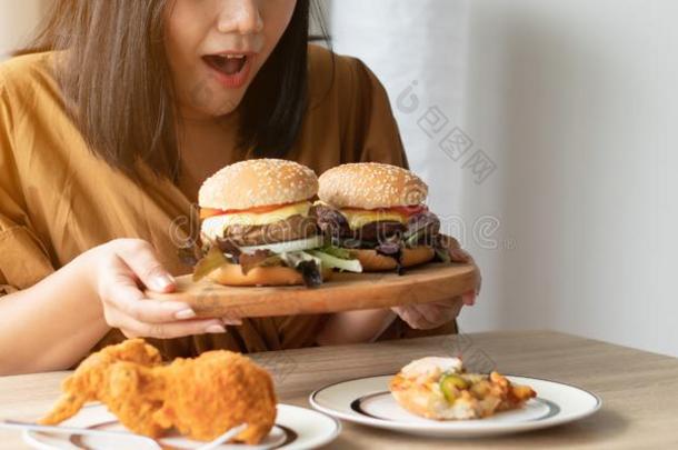 饥饿的超重的女人佃户租种的土地汉堡包向木制的盘子,喝醉了的