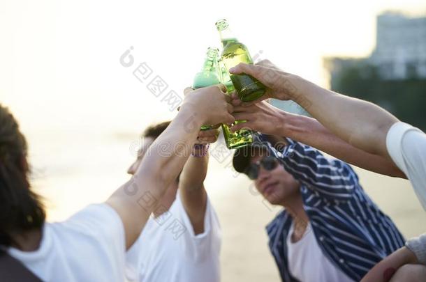 年幼的亚洲人成熟的人喝饮料啤酒和向<strong>祝酒</strong>向海滩