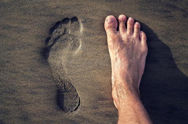 人脚印和赤脚的脚采用棕色的黄色的沙海滩波黑