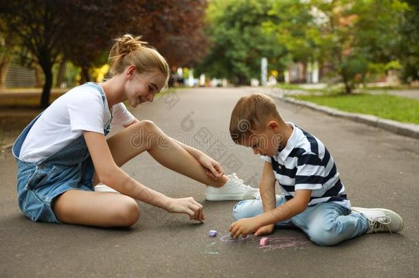 青少年保姆和漂亮的小的男孩和制造白色或彩色粉笔的白垩向沥青