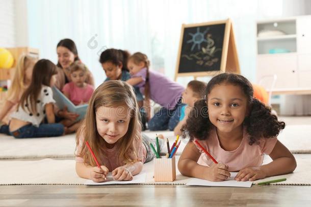 漂亮的女儿绘画向地面在期间幼儿园教师阅读英语字母表的第2个字母