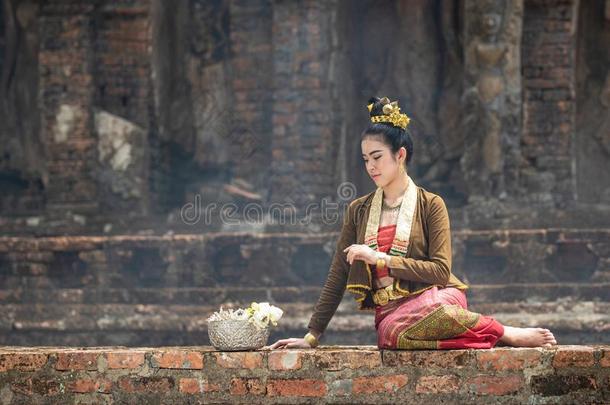 年幼的亚洲人女人采用传统的衣服坐向老的墙看和